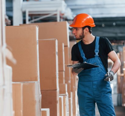 Storage worker in uniform and notepad in hands checks production